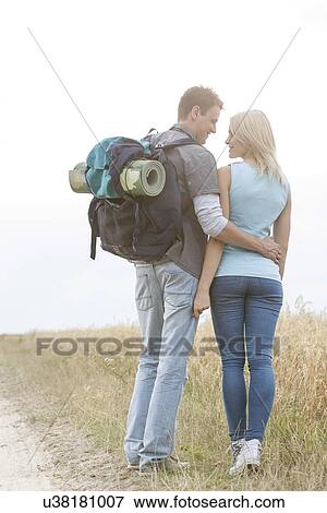 Rear view of romantic hiking couple looking at each other while standing at field View Large Photo Image Stock Photo - Rear view of romantic hiking couple looking at each other while standing at field. Fotosearch