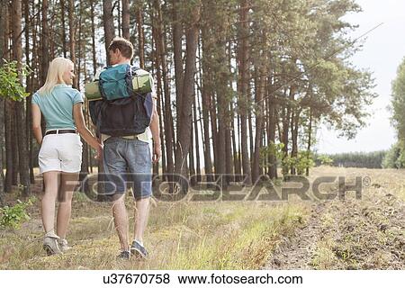 Rear view of young couple holding hands while hiking in forest View Large Photo Image Stock Photo - Rear view of young couple holding hands while hiking in forest. Fotosearch
