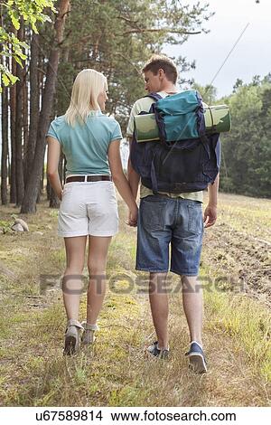 Rear view of young hiking couple holding hands while walking in countryside View Large Photo Image Picture - Rear view of young hiking couple holding hands while walking in countryside. Fotosearch
