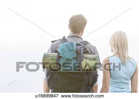 Stock Photo - Rear view of young hiking couple standing against clear sky. Fotosearch