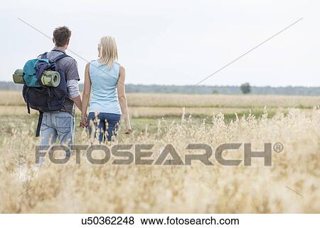 Rear view of young hiking couple walking through field View Large Photo Image Stock Photo - Rear view of young hiking couple walking through field. Fotosearch