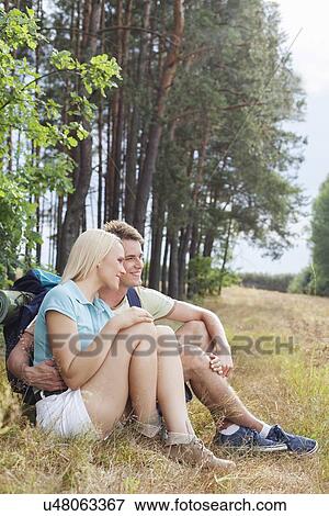 Stock Photo - Romantic hiking couple looking away while relaxing in forest. Fotosearch