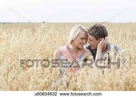 Romantic young couple looking at each other while relaxing amidst field View Large Photo Image Stock Image - Romantic young couple looking at each other while relaxing amidst field. Fotosearch