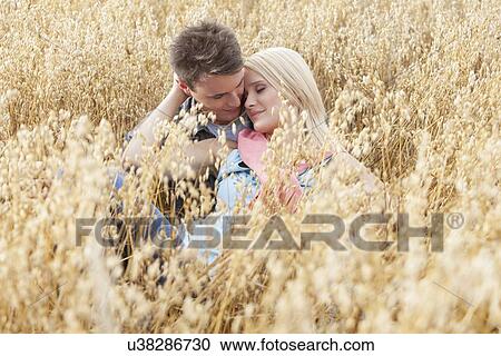 Stock Image - Romantic young couple relaxing amidst field. Fotosearch