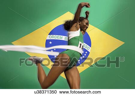 Stock Image - Runner Breaking through the finishing line tape over Brazilian flag. Fotosearch