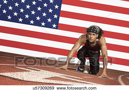 Stock Photo - Runner on a track in starting block in front of US flag. Fotosearch