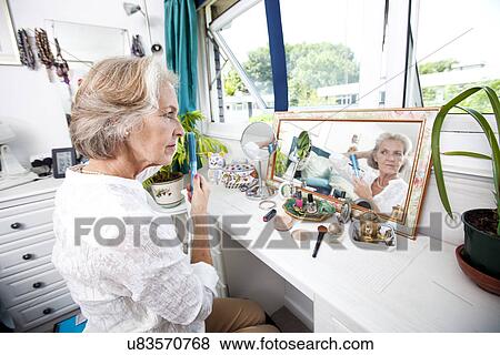 Stock Photo - Senior woman combing her hair at dresser in house. Fotosearch