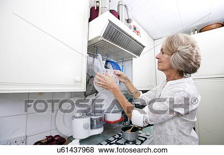 Stock Photo - Senior woman hanging colander in domestic kitchen. Fotosearch