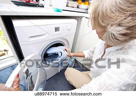 Stock Photography - Senior woman loading towel in washing machine at home. Fotosearch