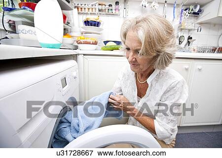 Stock Photo - Senior woman loading washing machine at home. Fotosearch