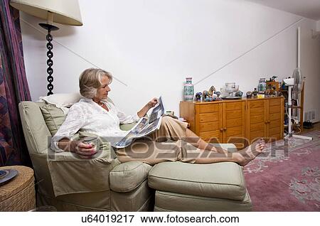 Senior woman reading newspaper while relaxing on armchair at home View Large Photo Image Stock Photo - Senior woman reading newspaper while relaxing on armchair at home. Fotosearch