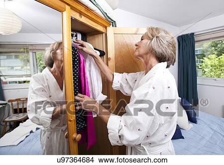 Picture - Senior woman selecting clothes from closet at home. Fotosearch