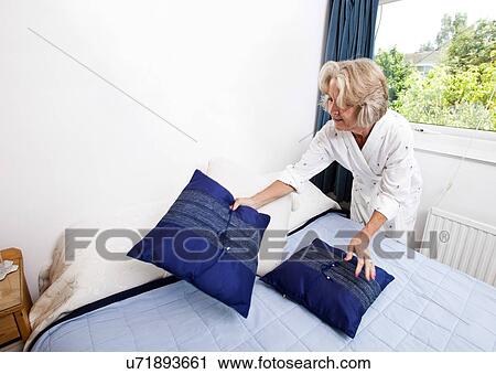 Senior woman setting up cushions on bed at home View Large Photo Image Stock Image - Senior woman setting up cushions on bed at home. Fotosearch