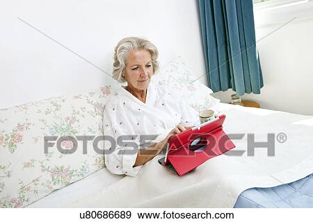 Senior woman using digital tablet on bed at home View Large Photo Image Stock Photo - Senior woman using digital tablet on bed at home. Fotosearch