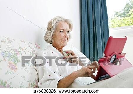 Senior woman using digital tablet while having coffee on bed at home View Large Photo Image Stock Photograph - Senior woman using digital tablet while having coffee on bed at home. Fotosearch