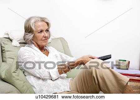 Senior woman using remote control while relaxing on armchair at home View Large Photo Image Stock Image - Senior woman using remote control while relaxing on armchair at home. Fotosearch