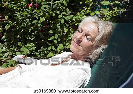 Stock Image - Senior woman with eyes closed relaxing on lounge chair in garden. Fotosearch