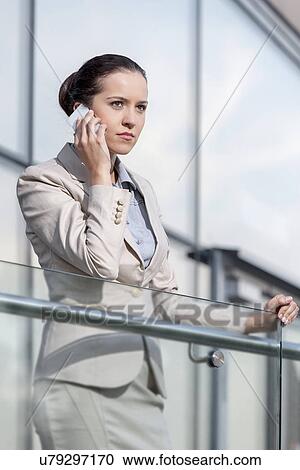 Serious young businesswoman using smart phone at office railing View Large Photo Image Stock Image - Serious young businesswoman using smart phone at office railing. Fotosearch