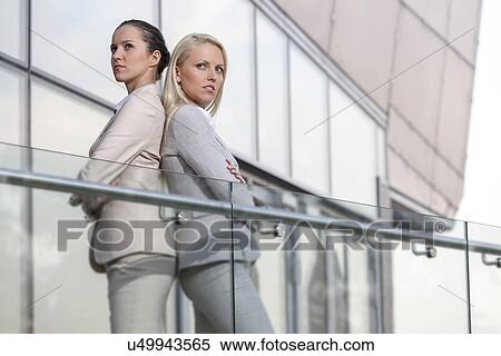 Serious young businesswomen standing back to back at office railing View Large Photo Image Stock Photography - Serious young businesswomen standing back to back at office railing. Fotosearch