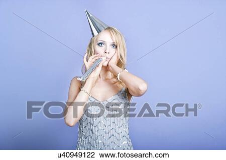 Stock Image - Sexy blonde party girl wearing silver dress and blowing party whistle. Fotosearch