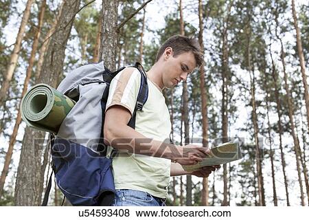 Stock Photo - Side view of young man with backpack reading map in woods. Fotosearch