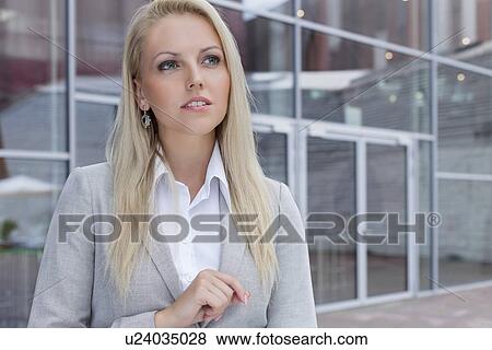 Stock Photo - Thoughtful businesswoman looking away against office building. Fotosearch