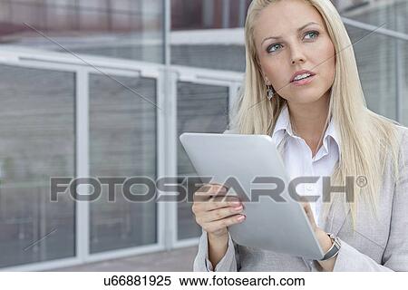 Thoughtful businesswoman using digital tablet while looking away against office building View Large Photo Image Stock Photography - Thoughtful businesswoman using digital tablet while looking away against office building. Fotosearch