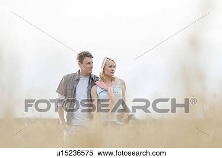 Thoughtful young couple looking away while standing at field View Large Photo Image Stock Photography - Thoughtful young couple looking away while standing at field. Fotosearch
