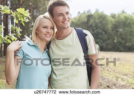 Stock Image - Thoughtful young couple smiling while hiking in forest. Fotosearch