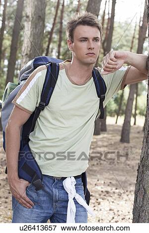Stock Photo - Thoughtful young man with backpack in woods. Fotosearch