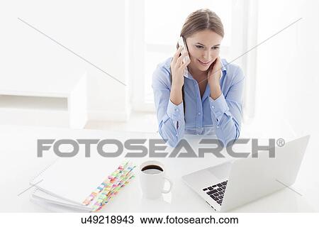 Stock Image - Woman using cell phone and looking at computer. Fotosearch