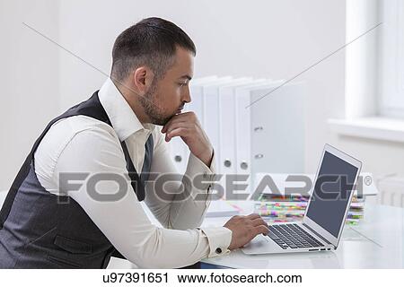Stock Image - Young businessman using at laptop at desk. Fotosearch