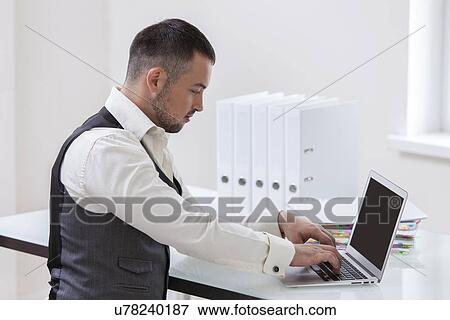 Young businessman using at laptop at desk View Large Photo Image Stock Photo - Young businessman using at laptop at desk. Fotosearch