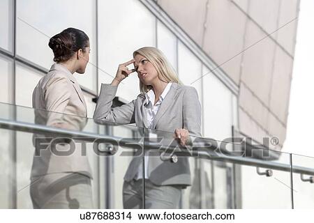 Picture - Young businesswoman arguing with female colleague at office railing. Fotosearch