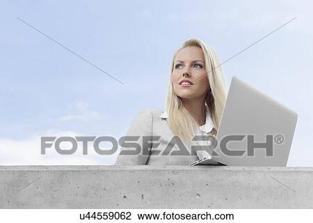Young businesswoman with laptop looking away on terrace against sky View Large Photo Image Stock Image - Young businesswoman with laptop looking away on terrace against sky. Fotosearch