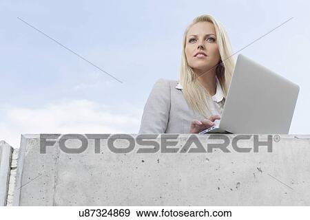 Young businesswoman with laptop looking away on terrace against sky View Large Photo Image Stock Photo - Young businesswoman with laptop looking away on terrace against sky. Fotosearch
