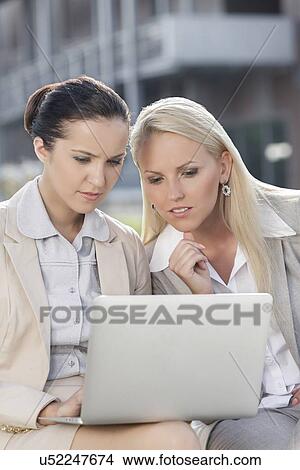 Young businesswomen working on laptop together while sitting outdoors View Large Photo Image Picture - Young businesswomen working on laptop together while sitting outdoors. Fotosearch