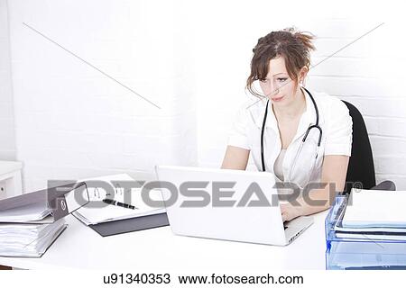 Young female doctor using laptop at desk in clinic View Large Photo Image Stock Image - Young female doctor using laptop at desk in clinic. Fotosearch