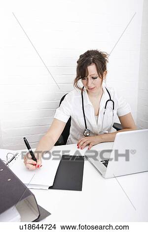 Young female doctor writing notes on desk in clinic View Large Photo Image Picture - Young female doctor writing notes on desk in clinic. Fotosearch