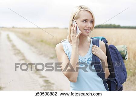 Young female hiker using mobile phone while standing on field View Large Photo Image Stock Image - Young female hiker using mobile phone while standing on field. Fotosearch