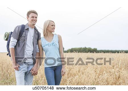 Stock Photo - Young hiking couple holding hands while standing on field. Fotosearch