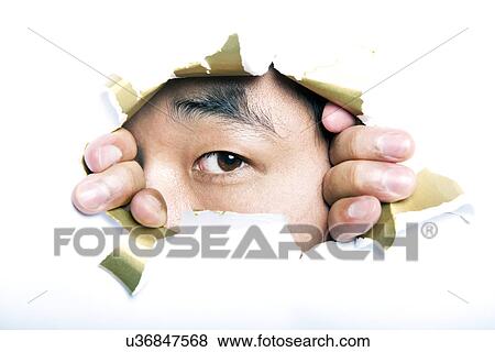 Stock Photo - Young Korean man looking through ripped paper hole. Fotosearch