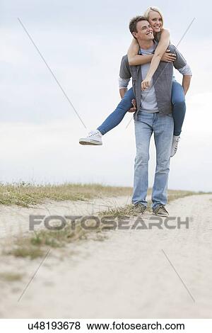 Stock Photo - Young man piggybacking woman on trail at field. Fotosearch