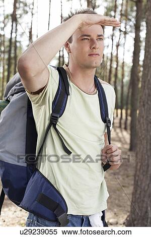 Young man with backpack shielding eyes in forest View Large Photo Image Stock Photography - Young man with backpack shielding eyes in forest. Fotosearch