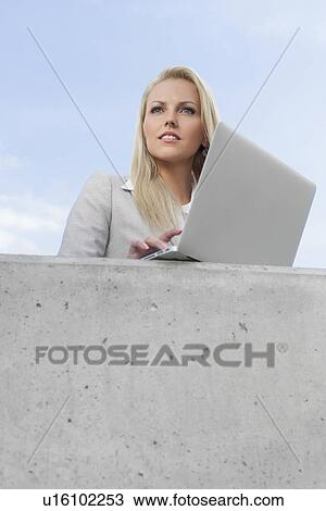 Young thoughtful businesswoman with laptop looking away while standing on terrace against sky View Large Photo Image Stock Image - Young thoughtful businesswoman with laptop looking away while standing on terrace against sky. Fotosearch