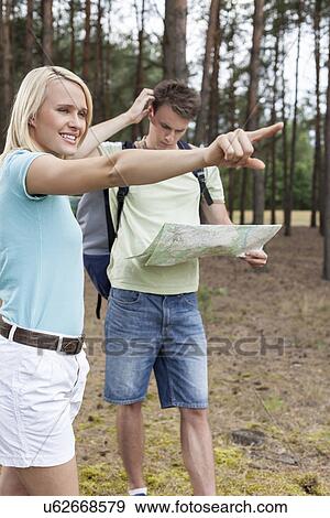 Stock Photo - Young woman pointing away with confused man holding map in forest. Fotosearch