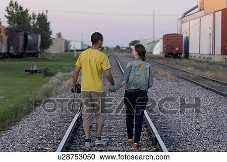 Stock Image - Couple walking between railroad tracks, Manitoba, Canada. Fotosearch