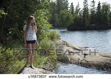 Stock Photo - Girl standing on a rock at the lakeside, Lake of The Woods, Keewatin, Ontario, Canada. Fotosearch