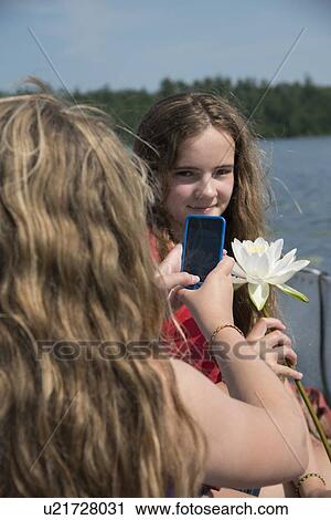 Stock Image - Girl taking a picture of her friend, Lake of The Woods, Keewatin, Ontario, Canada. Fotosearch