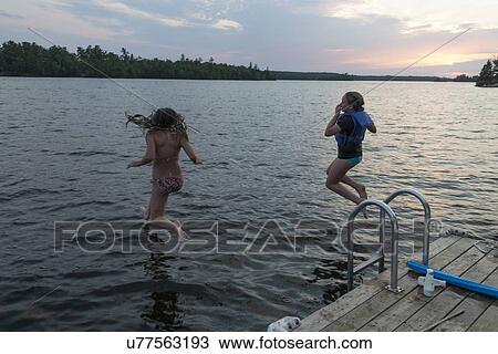 Stock Image - Girls jumping into a lake, Lake of The Woods, Keewatin, Ontario, Canada. Fotosearch